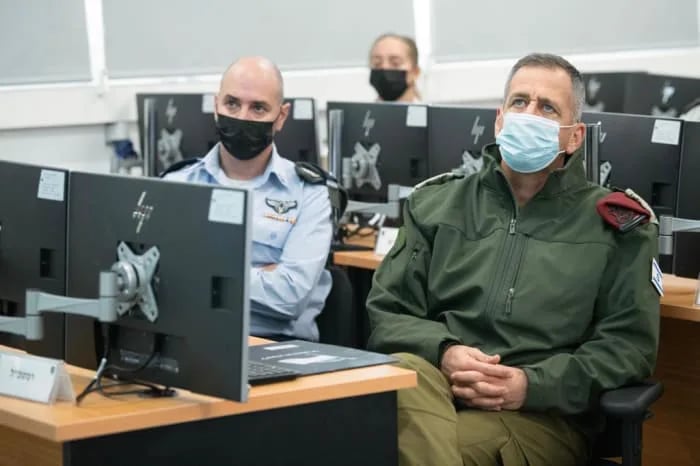 שני אנשים עוטים מסכות יושבים ליד מחשבים בחדר עם אחרים, ככל הנראה עוסקים בסביבת הכשרה או עבודה.